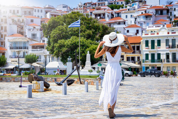 A tourist woman in a white summer dress explores the beautiful town of Skopelos island, Sporades,...