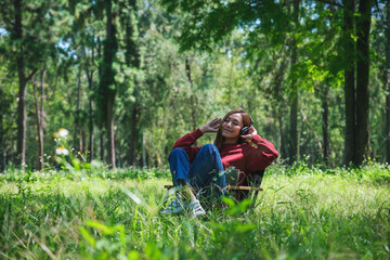 Naklejka na ściany i meble Portrait of a beautiful young asian woman enjoy listening to music with headphone while sitting on a camping chair in the park
