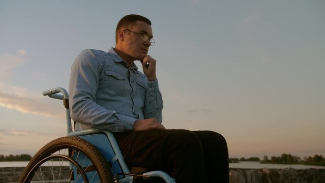 man in a wheelchair and glasses looks off into the distance in the hope of recovery.Disabled young guy in glasses wants to get out of his wheelchair and live normally.