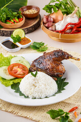 Bebek Bakar or Roasted duck with Sambal Terasi, a traditional food from Indonesia typical of West Java. This food is served with rice, cucumber, tomato and fresh vegetables.