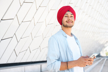 Smart inspired male Indian entrepreneur wearing red traditional headwrap turban using laptop...