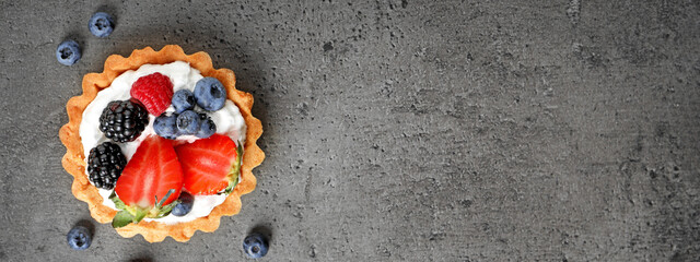 Tasty tartlet with fresh berries on grey table, top view with space for text. Banner design © New Africa