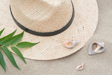 Fototapeta na wymiar Straw hat, seashells and green leaves on sandy beach, flat lay