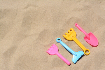 Fototapeta na wymiar Bright plastic rakes and shovel on sand, space for text. Beach toys