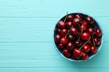 Fresh ripe cherries in bowl on turquoise wooden table, top view. Space for text