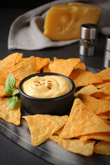 Delicious nachos and cheese sauce with basil on black table