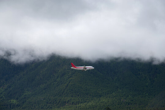 Airplane flying through the clouds over the pine forest covered mountains