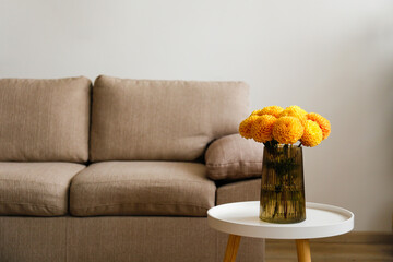 Close up shot of bouquet of beautiful yellow dahlia flowers in a glass vase and brown textile couch on the background. Copy space, close up, natural light.