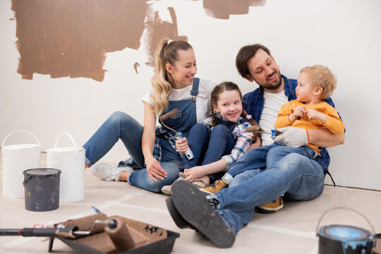 very cute family dressed in denim style sitting on the floor. Repairs are taking place around them. They are happy and discuss whether everyone likes the new brown wall color.