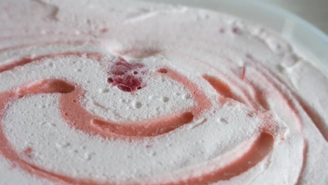 Close up view 4k stock video footage of tasty frozen white and pink fruit ice cream spinning around slowly. Textured dessert food background