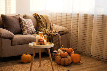 Bunch of pumpkins of different kinds, shapes and colors on the floor and a table near the couch of...
