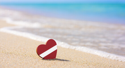 Flag of Latvia in the shape of a heart on a sandy beach. The concept of the best vacation in Latvia...