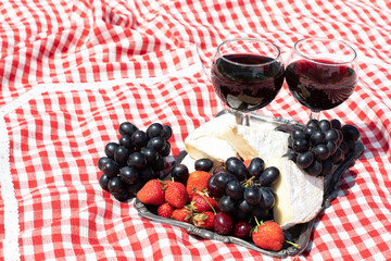summer picnic on a green lawn with red wine, cheese and fresh berries, grapes