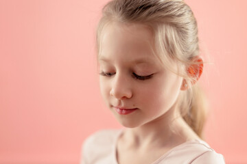 closeup portrait of Caucasian tender shy young girl ballerina on pink background