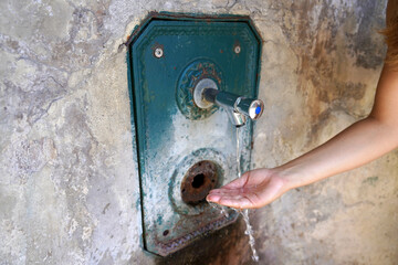 Close up of woman hand under running water from a fountain in the wall. Thirsty and water crisis...