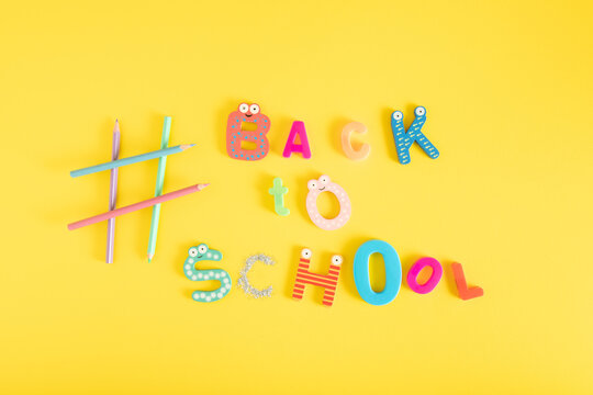 Back to school minimal creative design made of plastic toy letters and wooden crayons on a vibrant yellow background. Flat lay education background.