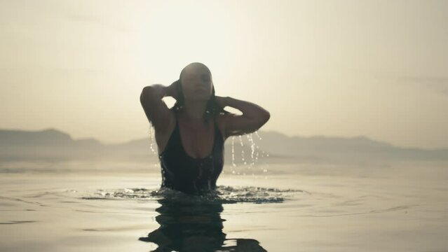 Slow motion video of a girl after swimming raises her head from the ocean water at sunrise. Beautiful nature and a woman coming out of the water after swimming in the sea. High quality 4k footage