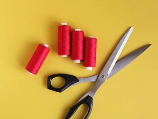 Four spools of pink thread, tailor's scissors on a yellow background. Top view
