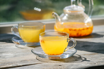 Sea buckthorn tea in glass cups and a glass teapot on a wooden windowsill. Healthy vitamin drink