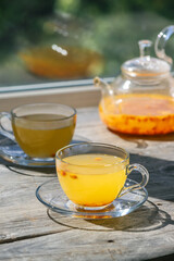 Sea buckthorn tea in glass cups and teapot on a wooden windowsill. Healthy vitamin drink