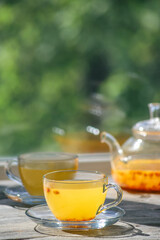 Sea buckthorn tea in glass cups and teapot on a wooden windowsill. Healthy vitamin drink