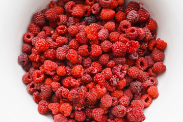 Top view red ripe raspberries picked from garden in white bowl, close-up