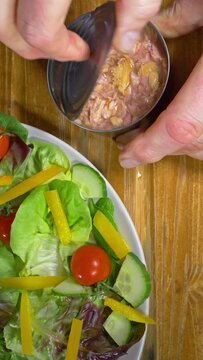 Vertical video social media format &ndash; Closeup overhead shot of a man&rsquo;s hands removing a can opener then the lid from a tin of chopped skipjack tuna in water, next to a plate of salad.
