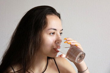 Pretty young girl with long hair drinking clean water, glass in female hands close up. Concept of...