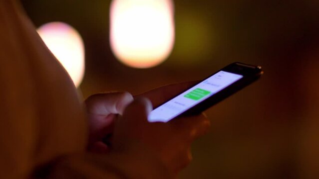 Woman Typing on Smartphone Touchscreen Keyboard on Bokeh Background at Night