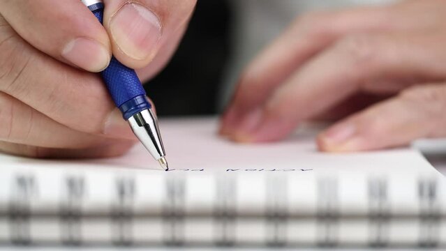 Concept of writing on paper, letter, pen, notepad, diary. Close up hand writing paper on notebook with blue pen to note, memo, list action plan at office or home desk, selective focus 4k resolution.