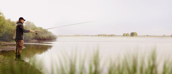 A fisherman in a jacket with a fishing rod stands on the bank of the river. Fishing in the river....