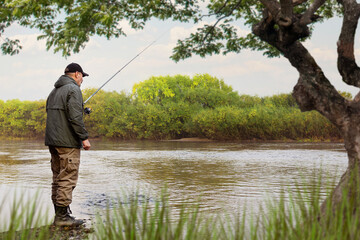 A fisherman in a jacket with a fishing rod stands on the bank of the river. Fishing in the river....
