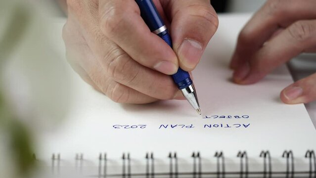 Concept of writing on paper, letter, pen, notepad, diary. Close up hand writing paper on notebook with blue pen to note, memo, list action plan at office or home desk, selective focus 4k resolution.