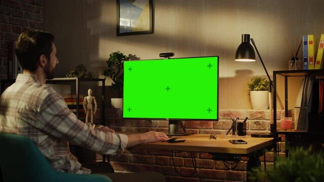 Office Employee Working from Home, Talking on Video Call on Desktop Computer with Monitor with Green Screen Mock Up. Man Sitting in Living Room, Chatting Online with Friends and Family in the Evening.