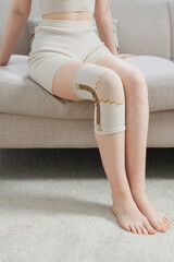 Knee support brace on a woman leg. girl in an orthosis in the interior of the house. Orthopedic...