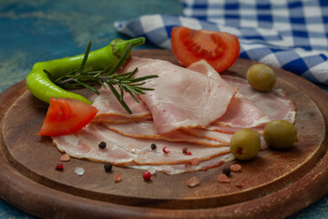 Spicy pork ham slices on wooden board. Sliced prosciutto with hot chilli, tomato and olives. Top view.