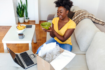 Excited african young woman shopper opening parcel box at home. Happy satisfied ethnic girl customer receiving online shop purchase by postal shipping, unpacking delivery receiving gift sit on sofa.