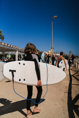 Chico joven con tabla de surf andando hacia la playa en zona de escuelas de surf