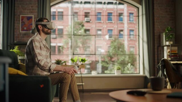 Adult Bearded Male Using Virtual Reality Headset and Controllers at Home. Creative Man Sitting on a Sofa in Living Room, Playing VR Video Game or Working with Special Digital Tools.