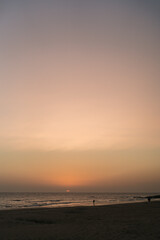 Atardecer en la playa con el sol y horizonte anaranjados con escenas de transeúntes y pescadores