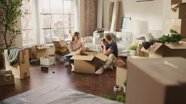 Happy Young Homeowners Moving In: Happy Couple Sitting on the Floor of the Newly Purchased Apartment Unpacking Cardboard Boxes. Mortgage Loan, Real Estate, Home Sweet Home for Young Family