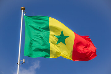 The flag of Senegal flies against a clear blue sky with white clouds. Close-up, perfect for news.
