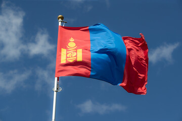 The Mongolian flag flies against a clear blue sky with white clouds. Close-up, perfect for news.
