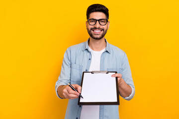 Photo of young guy smiling holding notepad pen waiting you signature write for new delivery isolated on yellow color background