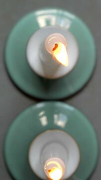 Vertical video social media format – Closeup dolly shot of two burning wax candles in green holders, standing next to each other, with focus on the wicks and flickering flames.