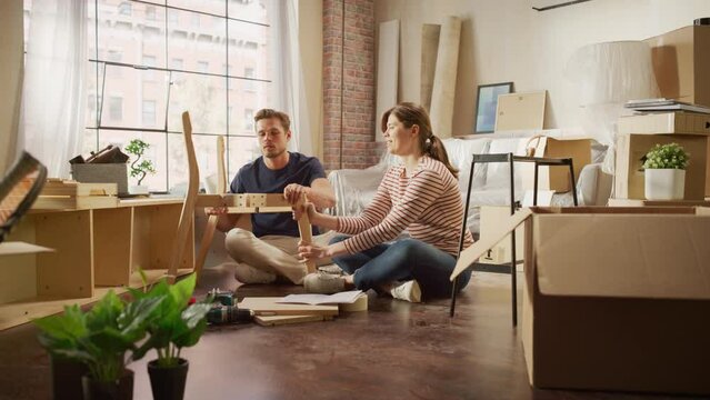 Family Moving in and Home Renovations: Happy Couple Assembles Furniture Together, Girlfriend Reads Instructions and Boyfriend Follows them with some Force. New Apartment for Young Partners in Love