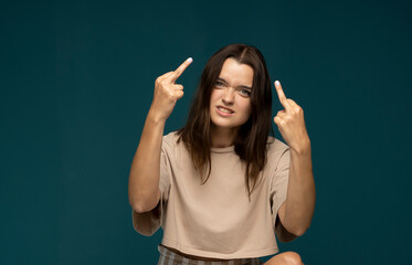 Portrait of brunette student woman showing middle finger doing rebel expression at camera standing in studio with blue background.