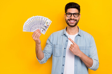 Photo of cheerful guy banker hands hold cash finger point usd money isolated on yellow color...