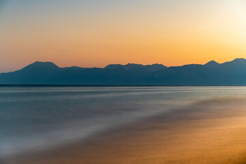Long exposure, the sea against the background of mountains. Sunset and clear sky.