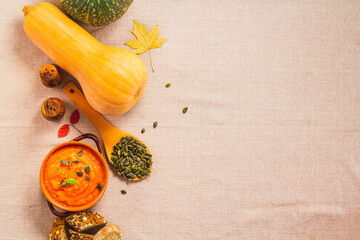 Pumpkin and carrot soup in clay bowls and organic pumpkins with black bread on a linen background....
